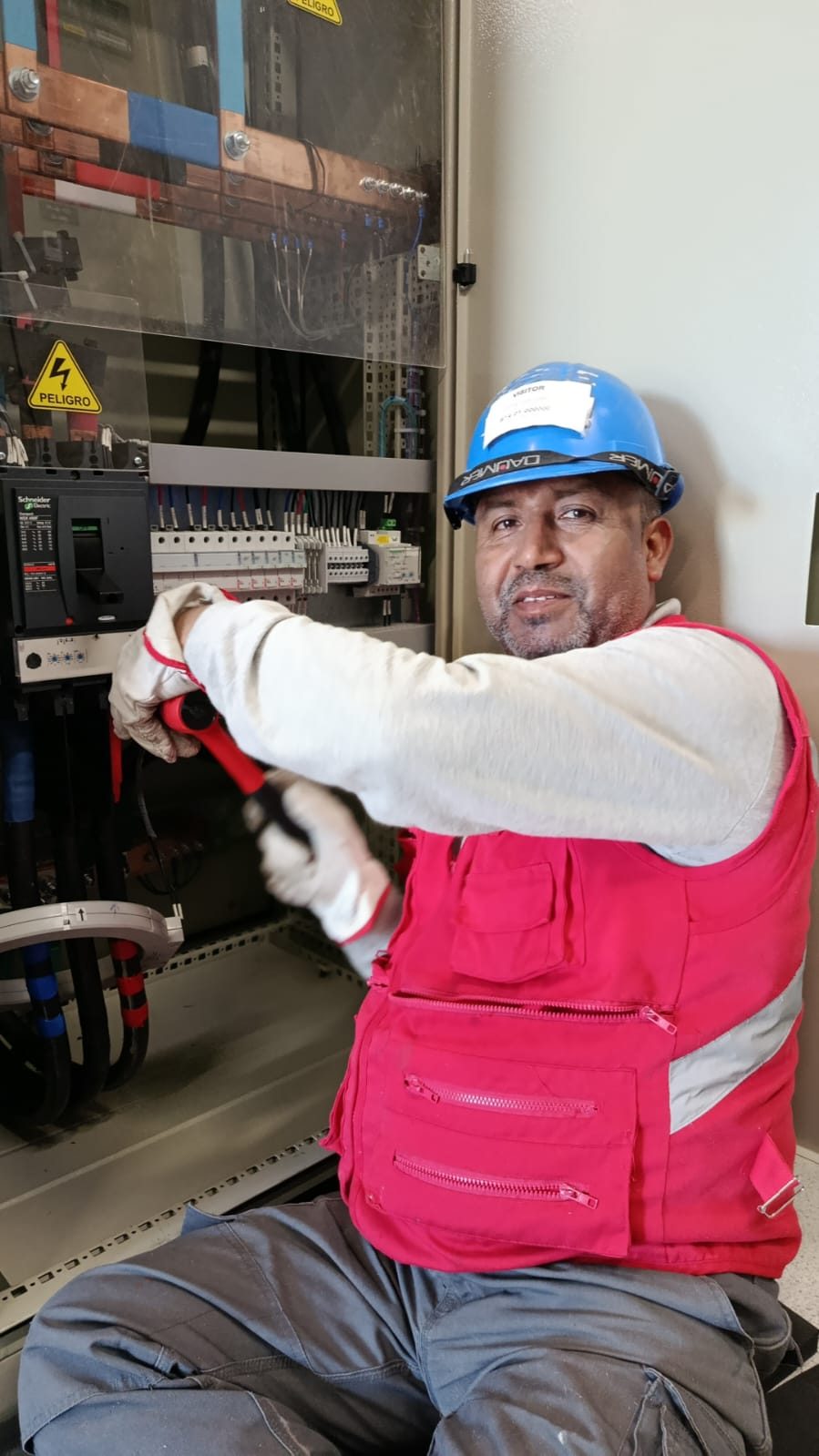 Técnico con casco y guantes trabajando en un tablero eléctrico